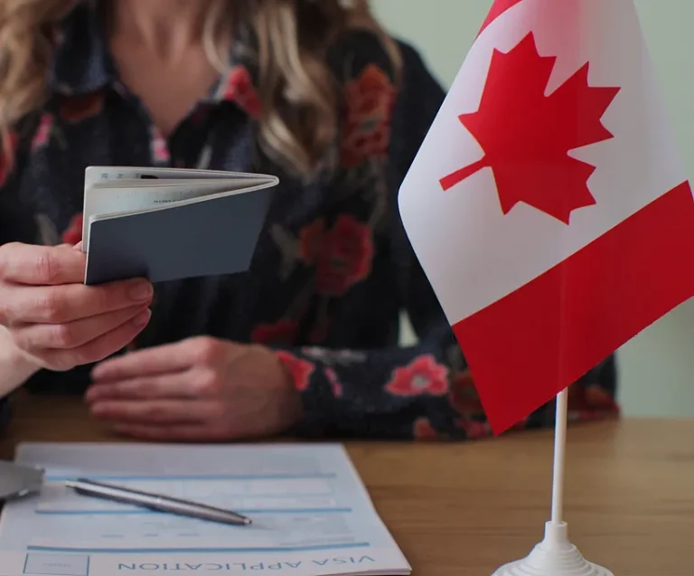 An immigration consultant returns an applicants passport with the visa application documents and Canadian flag on the desk.