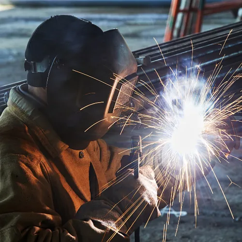 A man in a welding helmet performs welding, showcasing precision and dedication to his craft.