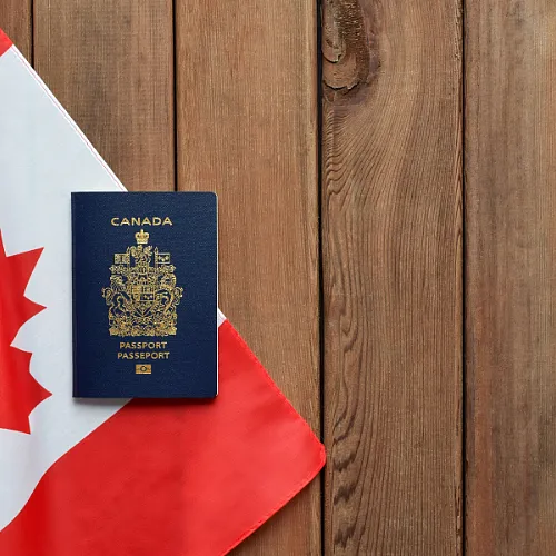A Canadian passport displayed on a Canadian flag with wooden background, highlighting its design and official insignia.