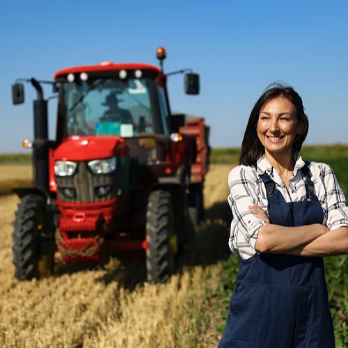 A woman stands before a tractor, representing her role in farming and the importance of machinery in agriculture.